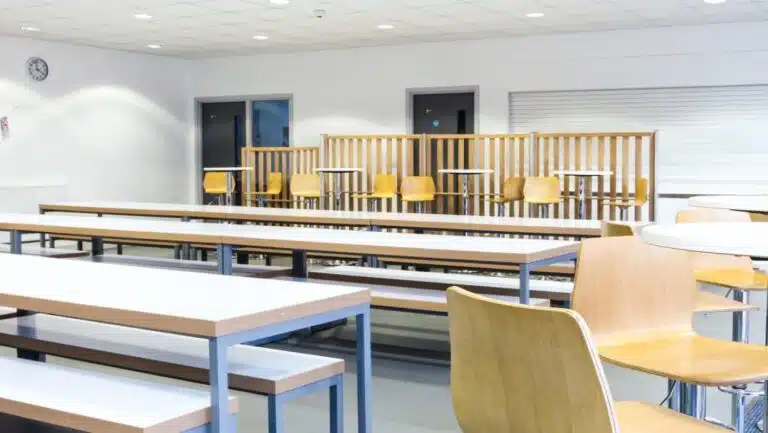 School dining hall with tables and seating options, including benches and chairs.